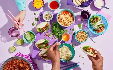 En festlig dukning med asiatiska frukter och bao buns. Färgglada skålar med mango, kimchi, jordnötter och grönsaker.