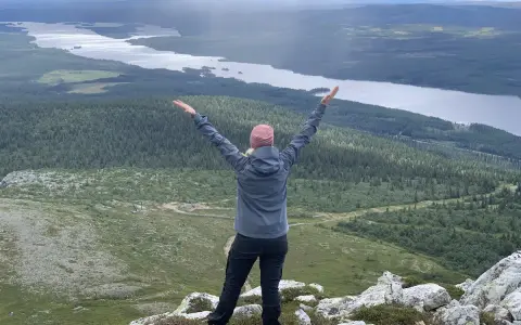 En person med armarna uppsträckta njuter av en fantastisk utsikt över sjöar och skogar under en Lofsdalen vandring.