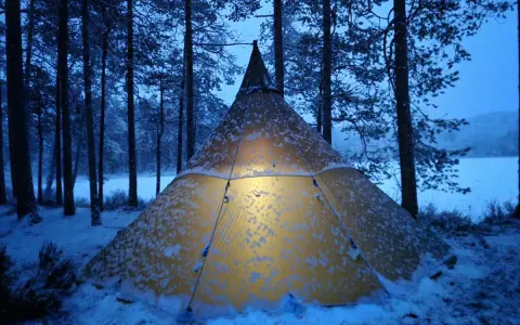 Varmt ljus lyser från ett snötäckt tält i Glaskogens naturreservat. En magisk vinterkväll.