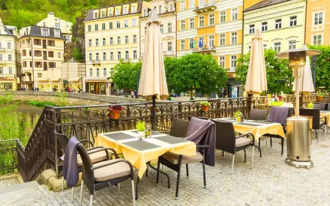Uteservering vid en flod i Karlovy Vary med gula byggnader i bakgrunden.