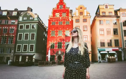 En kvinna med solglasögon står framför färgglada hus på ett torg. Kanske är detta sveriges vackraste stad?
