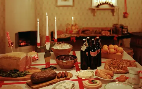 Julbord i Sverige med julmat som skinka, korv, risgrynsgröt och julmust. En tomte ljusstake lyser upp bordet.