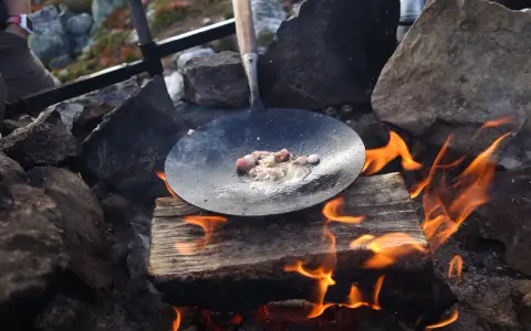 Stekt fläsk i stekpanna över öppen eld, en del av ett recept kolbullar. Elden sprakar och röken stiger.