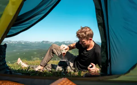 Man gör kaffe vid tältöppningen under en vandring i Sverige sommar. Vacker utsikt över fjällen.