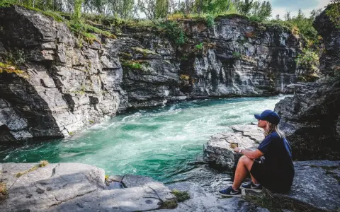 En person sitter vid en forsande turkos flod omgiven av klippor. Ett perfekt utflyktsmål i Mellansverige för naturupplevelser.
