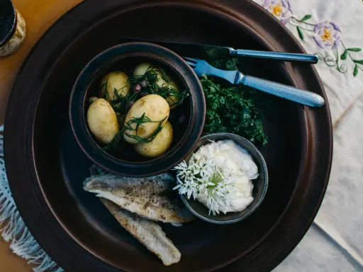 En rustik tallrik med nykokt färskpotatis, stekt fisk och en krämig sås. En härlig bit av finsk mat, redo att avnjutas.