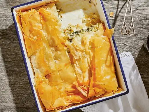 En gyllene, krispig spenatpaj i en blå kantad form. Perfekt för ett spanakopita recept.