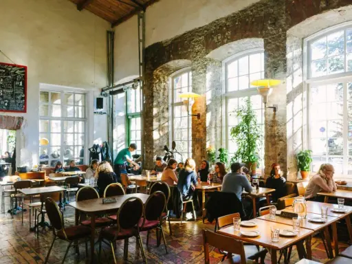 Folk äter och dricker på en livlig restaurang i Tallinn. Stora fönster släpper in solljus i lokalen med rustika tegelväggar.