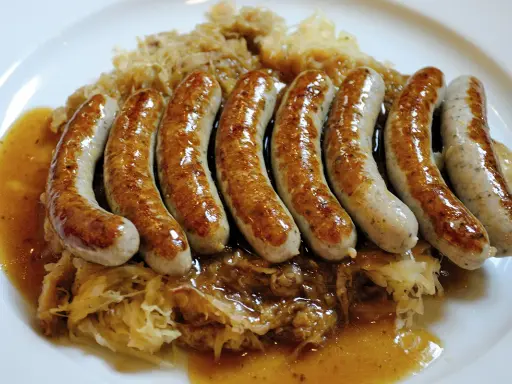 En tallrik med flera saftiga, gyllene tysk korv serverad på surkål med en smakrik sås.