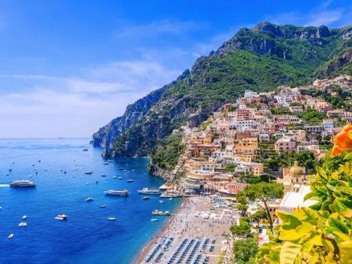Färgglada hus klättrar uppför bergssluttningen vid en livlig strand och blått hav. En vacker vy som ger fakta om Italien.