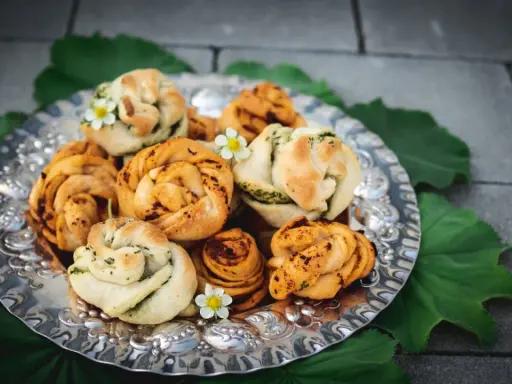 En silverbricka fylld med vackert formade vegetariska pizzabullar, dekorerade med små vita blommor och gröna blad.