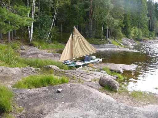 En liten segelbåt med åror ligger vid en stenig strand. En härlig plats att paddla Dalslands kanal på.