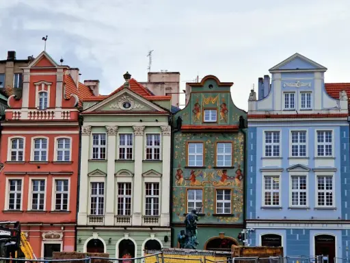 Färgglada husfasader i **Poznan, Polen**, med detaljerade ornament och tak. En byggkran syns i förgrunden.