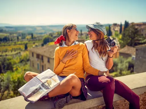 Två glada vänner njuter av sin resa i Europa, med en karta och kamera redo för nya äventyr i en vacker italiensk landskapsvy.