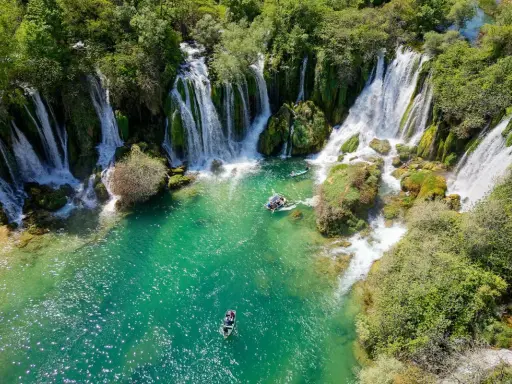 Vackra Kravice vattenfall med turkost vatten och båtar som glider fram. En idyllisk plats för avkoppling.
