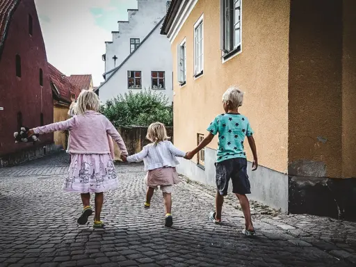 Tre barn håller varandra i handen på en kullerstensgata på Gotland, på väg mot äventyr.