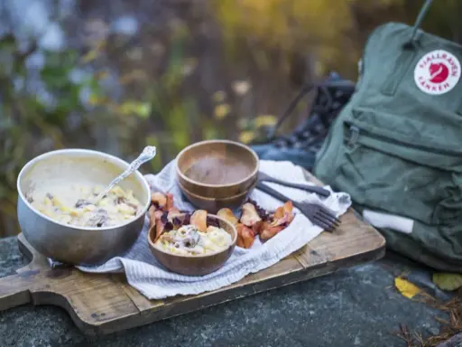 En härlig måltid med pasta och svamp, perfekt för att torka kyckling och njuta av naturen. En Fjällräven ryggsäck och vandringskängor syns i bakgrunden.