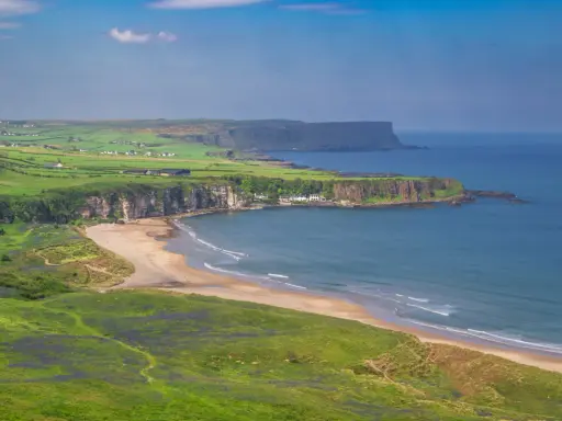 Grönskande kullar och en sandstrand vid havet på Irland, nära Belfast.