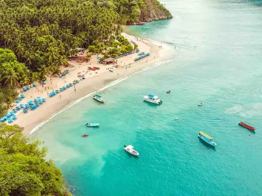 Vacker strand med turkost vatten, palmer och båtar. Perfekt för en resa till Costa Rica med tips om sol och bad.
