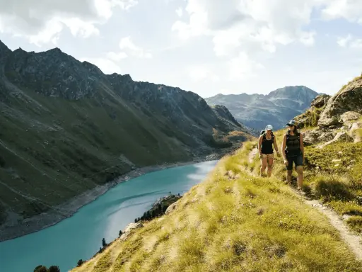 Två personer vandrar på en bergstig med en turkos sjö och dramatiska berg i bakgrunden. En perfekt dag för att vandra i Schweiz.