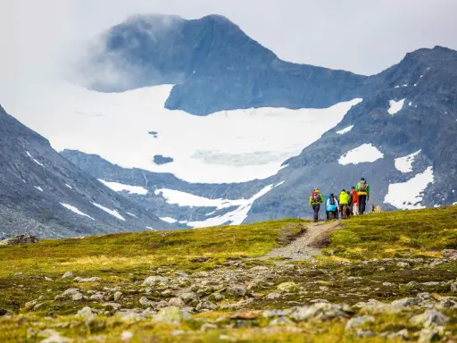 Vandringsgrupp på väg uppför en stenbelagd stig mot Sylarnas glaciärklädda toppar.