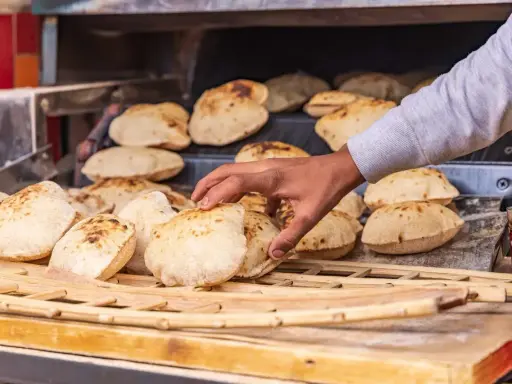 En hand tar färskt, fluffigt bröd från en ugn. Detta är en del av den autentiska egyptiska maten, perfekt för att doppa i läckra röror.