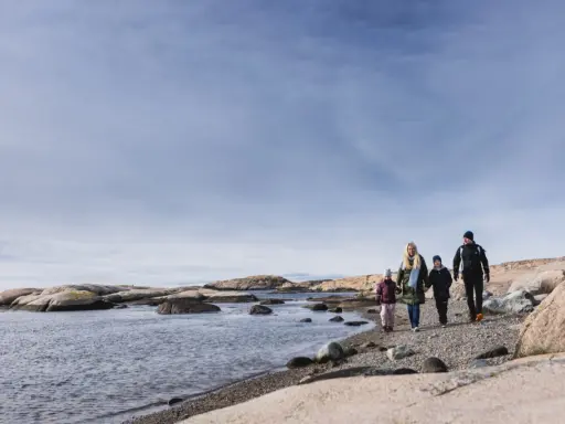 Familj promenerar längs en stenig strand vid Tjurpannans naturreservat.