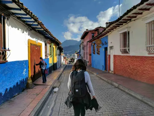 Färgglada hus i La Candelaria, Bogotá. En kvinna med ryggsäck går längs en kullerstensgata. Här finns fakta om Colombia.