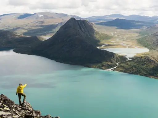 Vandrare pekar ut över turkost vatten och berg under en Besseggen vandring.