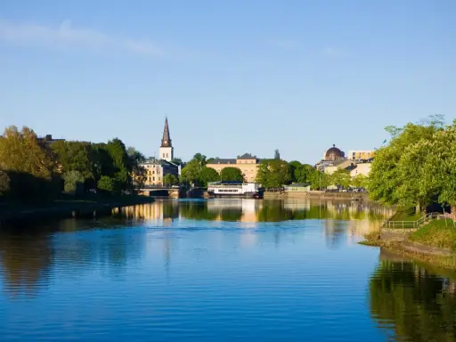 Vacker vy över Klarälven med stadens silhuett, kyrktorn och grönska. En perfekt plats att se i Karlstad en solig dag.