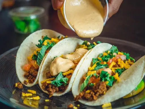 Tre läckra tacos med köttfärs, grönsaker och ost. En krämig sås hälls över dem, perfekt mexikansk mat.