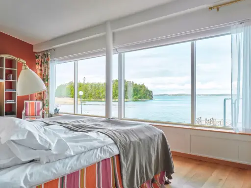 Sovrum med fantastisk havsutsikt, perfekt för ett bra hotell i Stockholm. Säng med vita lakan och grå pläd, färgglad randig sängkjol.