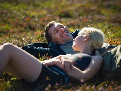 Ett par vilar i gräset efter en vandring i Vemdalen, skrattandes och njutandes av naturen.