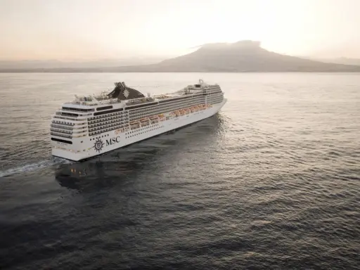 Kryssningsfartyget MSC Poesia glider fram på havet i solnedgången, med en vulkan i bakgrunden.