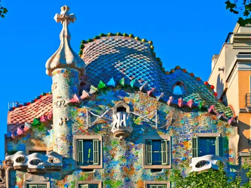 Färgglatt och fantasifullt **Gaudi hus Barcelona** med mosaiktak och unika balkonger under en klarblå himmel.