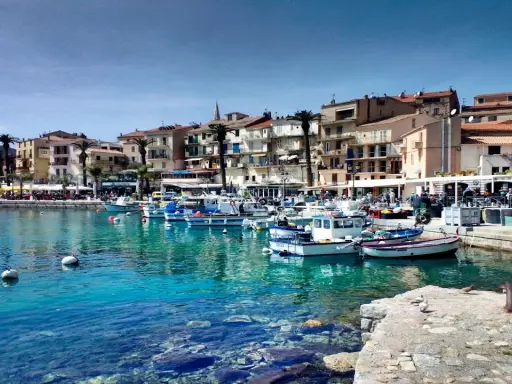 Båtar i en turkos hamn i Calvi, Korsika, med färgglada hus och palmer längs kajen.