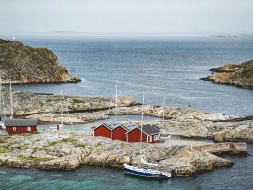 Röda sjöbodar och segelbåtar på klippor vid havet. En idyllisk bild av sommar i Sverige.