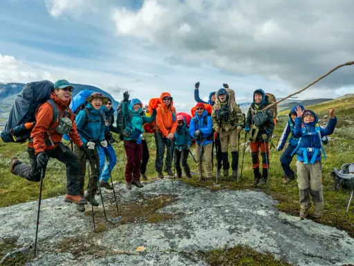 Glada vandrare, redo för Fjällräven Classic i svenska fjällen. De hoppar av glädje på en sten.
