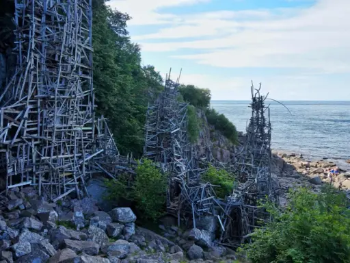 Nimis i Skåne: en skulptur av trä som klättrar uppför klipporna vid havet.