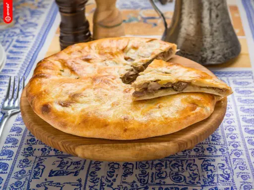 En gyllene, nybakad khachapuri, en klassisk georgisk mat, ligger på en träskärbräda. En bit är uppskuren och visar det smakrika köttfyllningen.