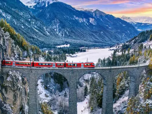 Röda tåget korsar en stenbro över en snöig dal i Schweiz. Fantastiska vyer för din resa till Schweiz tips.