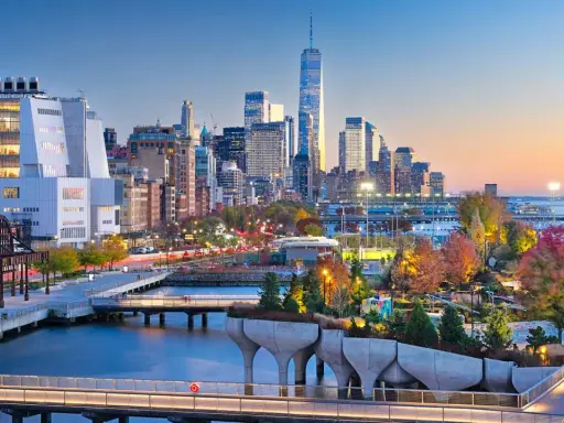 Fakta om New York: En vy över Manhattans skyline vid solnedgången, med den ikoniska One World Trade Center och en modern park vid vattnet.