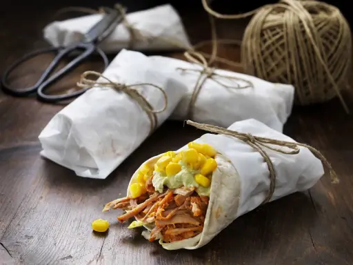 En läcker pulled pork wrap med majs och avokadokräm, inslagen i papper och bunden med snöre.