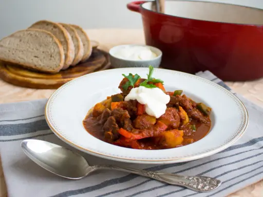 En portion mustig ungersk mat, en mustig gryta med kött och grönsaker, toppad med gräddfil och persilja. Serveras med gott bröd.