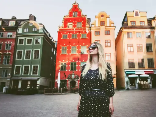En kvinna med solglasögon står framför färgglada hus på ett torg. Kanske är detta sveriges vackraste stad?