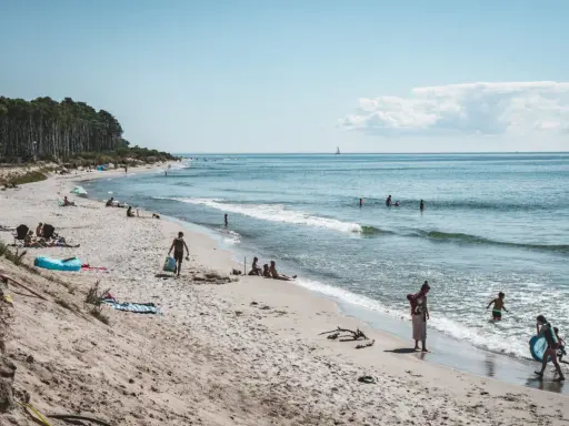 Människor njuter av solen och havet på sveriges finaste strand. Barn leker i vattnet medan andra kopplar av på sanden.