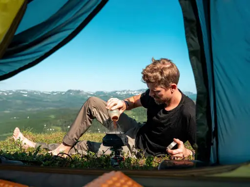 Man gör kaffe vid tältöppningen under en vandring i Sverige sommar. Vacker utsikt över fjällen.
