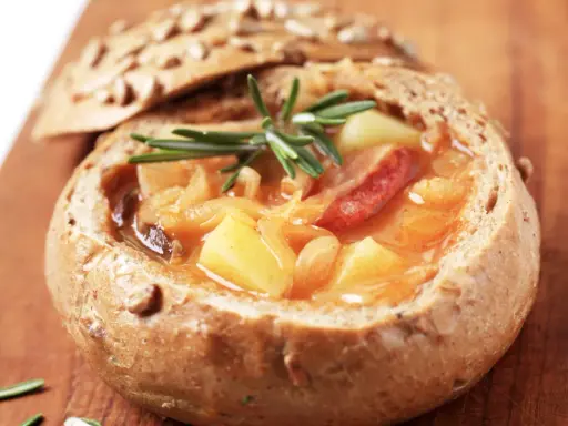 En mustig gryta med potatis och korv serveras i ett urgröpt bröd, en härlig tjeckisk matupplevelse.