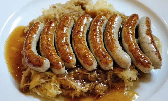 En tallrik med flera saftiga, gyllene tysk korv serverad på surkål med en smakrik sås.