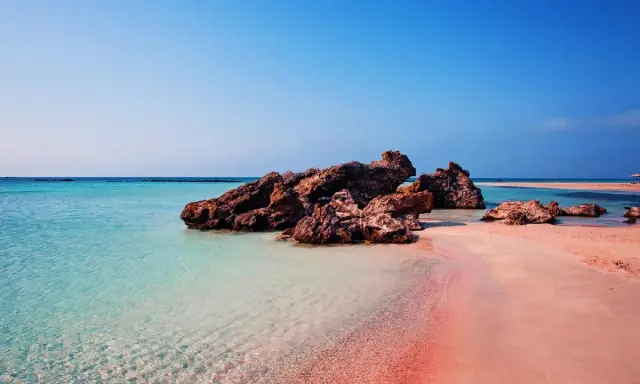 En rosa strand på Kreta med turkost vatten och klippor. En dröm för alla som älskar en kreta rosa strand.